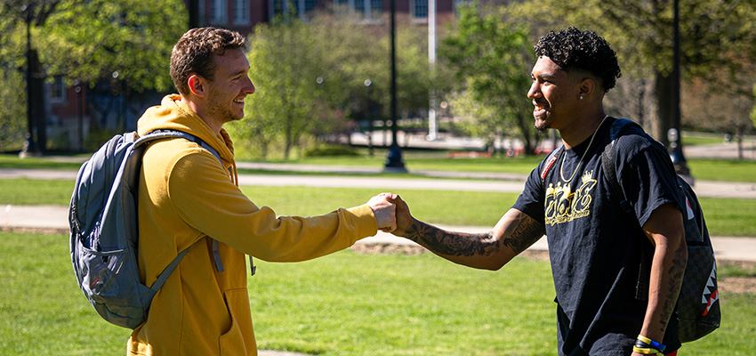 Students embrace with a handshake with Old Main in the background