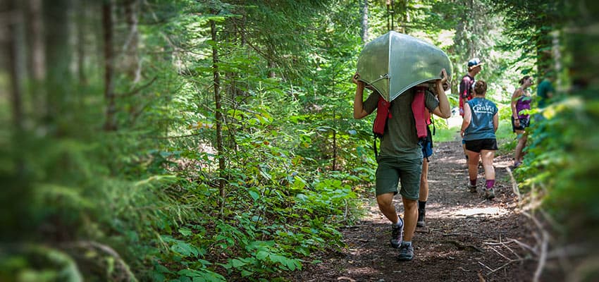 Student portaging a canoe through the woods