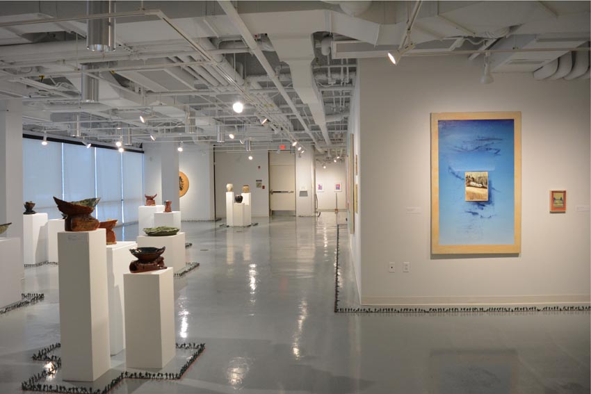 View into the central gallery at Dowd Gallery featuring sculptural objects produced by Jeremiah Donovan, professor of ceramics, Jillian McEvoy, instructor of ceramics, Jaroslava Prihodova, director of the Dowd Gallery, Hannah Hones, instructor of sculpture, paintings by Stephen Alexander Clark, processor of painting, and floor installation by Bryan Valentine Thomas, instructor of design and drawing, at the Art and Art History Department.