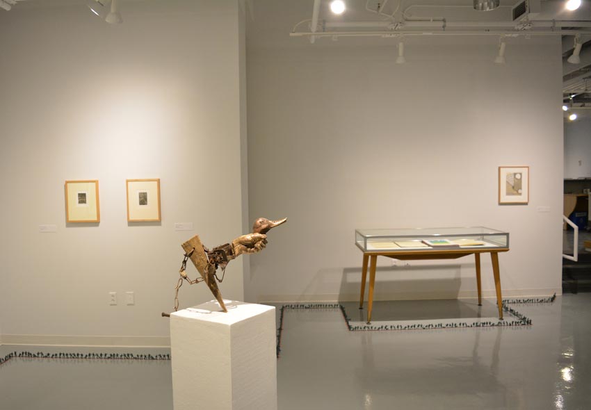 View into the west gallery at Dowd Gallery featuring sculpture produced by Scott Oldfield, instructor of drawing, prints by Charles Heasley, professor of printmaking and other courses, and floor installation by Bryan Valentine Thomas, instructor of design and drawing, at the Art and Art History Department. 